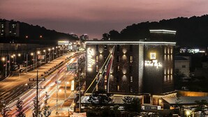 A multi-level building with a prominent 'B' sign, surrounded by a well-lit urban street at night. - Bellino Hotel (Osan)