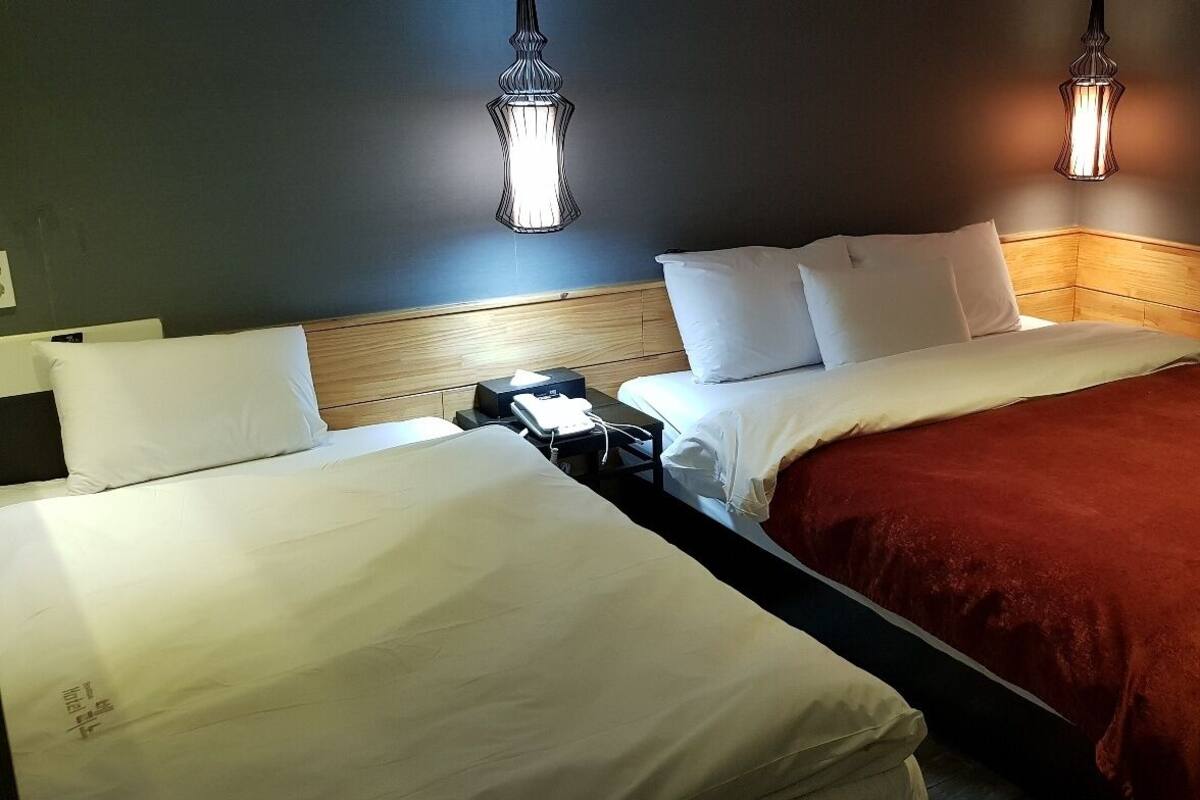 A hotel room with two beds, a wooden headboard, and two wall-mounted lamps.