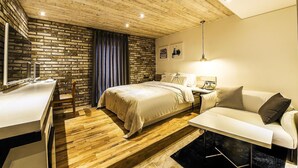 A modern bedroom with a brick wall, wooden ceiling, a bed, a desk, and a sofa. - Bellino Hotel (Osan)
