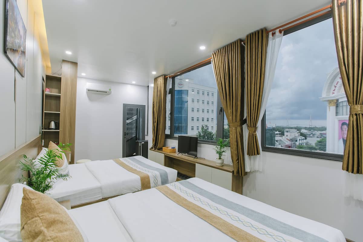 Hotellihuone, jossa on kaksi sänkyä, työpöytä tietokoneella, ikkuna verhoilla ja näkymä kaupunkimaisemaan.