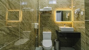 A modern bathroom with a marble wall, a white toilet, a sink, and a towel rack. - Peony Hotel (Can Tho)