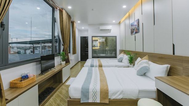 A hotel room with two beds, a TV, a window with curtains, and a view of a bridge. - Peony Hotel (Can Tho)