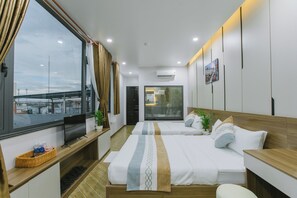 A hotel room with two beds, a TV, a window with curtains, and a view of a bridge. - Peony Hotel (Can Tho)