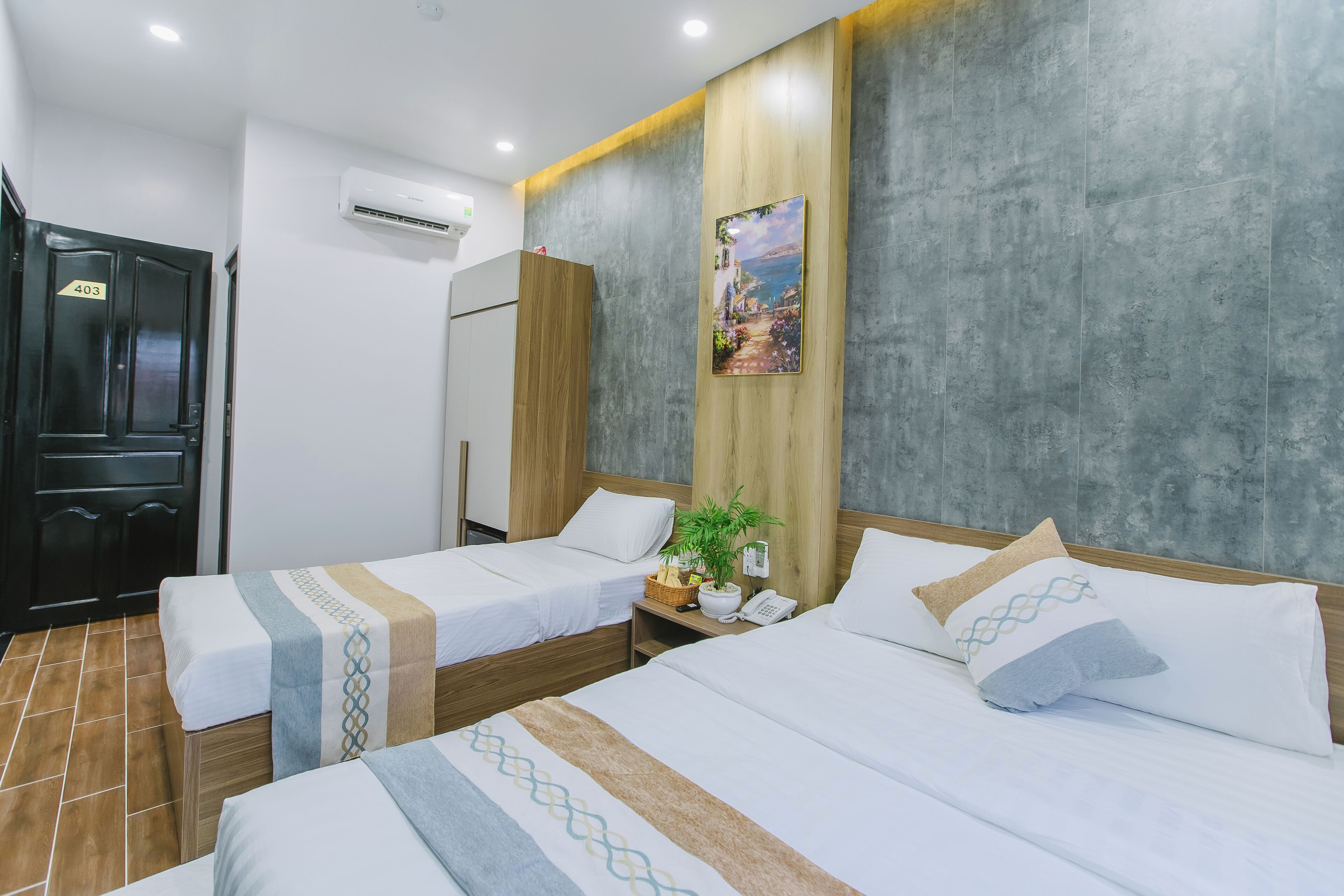 A hotel room with two beds, a wooden headboard, a painting, a plant, and a phone on the nightstand.