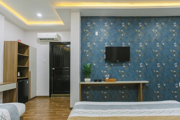 Une chambre d’hôtel avec un lit, un petit bureau agrémenté d’une plante, un téléviseur fixé au mur et une armoire.