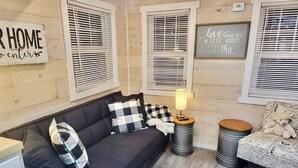Un salon chaleureux avec un canapé foncé, des coussins à carreaux, une petite table avec une lampe et des objets de décoration.