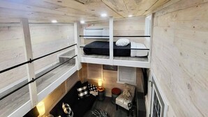 Une chambre avec un lit superposé, un plafond en bois, une petite table avec une lampe et une chaise.