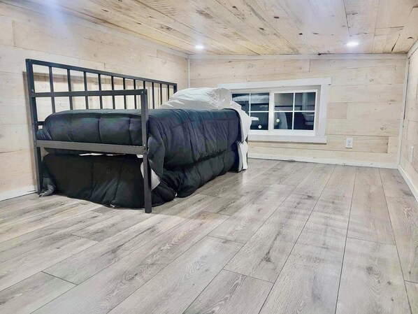 A room with a bunk bed, wooden flooring, a window with blinds, and a white wall.