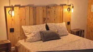 Quarto com cabeceira de madeira, duas luminárias de apoio, cama com roupa de cama estampada e um letreiro sobre a cama que diz "ATELIER DES REVES".