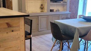 Uma área de refeições com uma mesa e cadeiras de madeira, uma estante com livros e uma televisão.