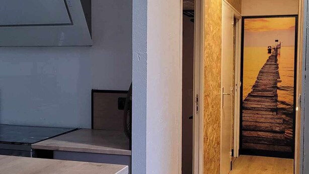 Um corredor com piso de madeira, uma sala de jantar com mesa e cadeiras, e uma porta que dá para um quarto com piso de madeira.