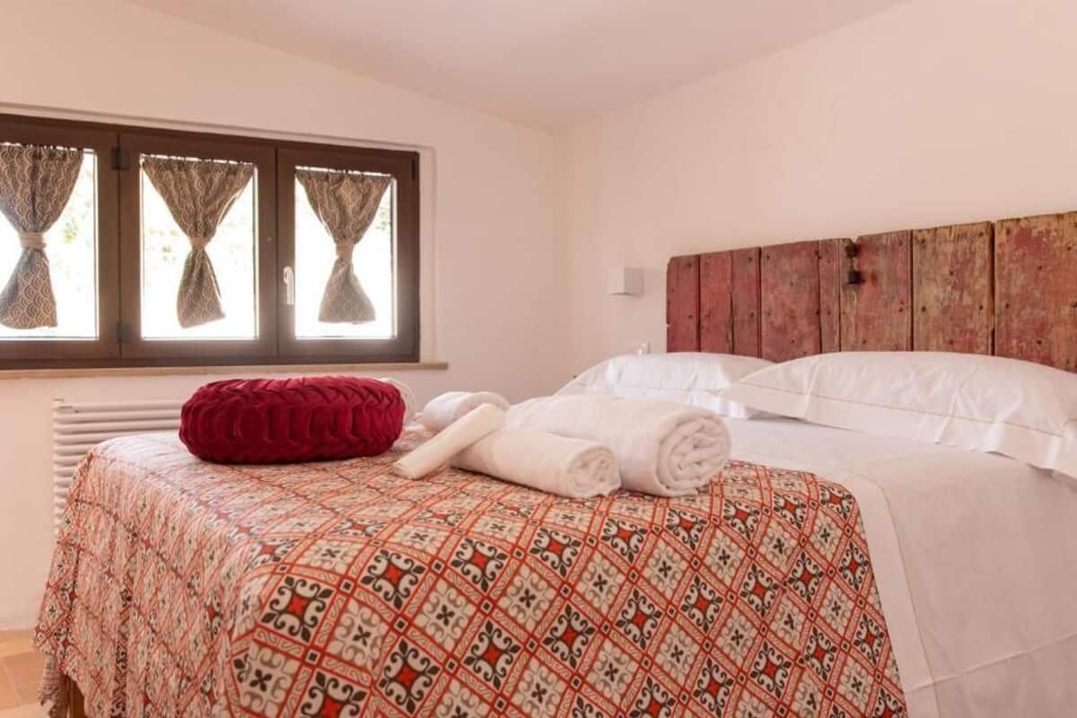 Un dormitorio con una colcha estampada, un cojín rojo y toallas dobladas con esmero.