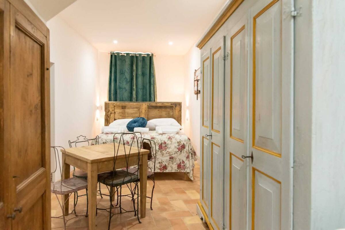 Un dormitorio pequeño y acogedor con cabecera de madera, cama con ropa de cama floral, cortina verde y armario de madera.