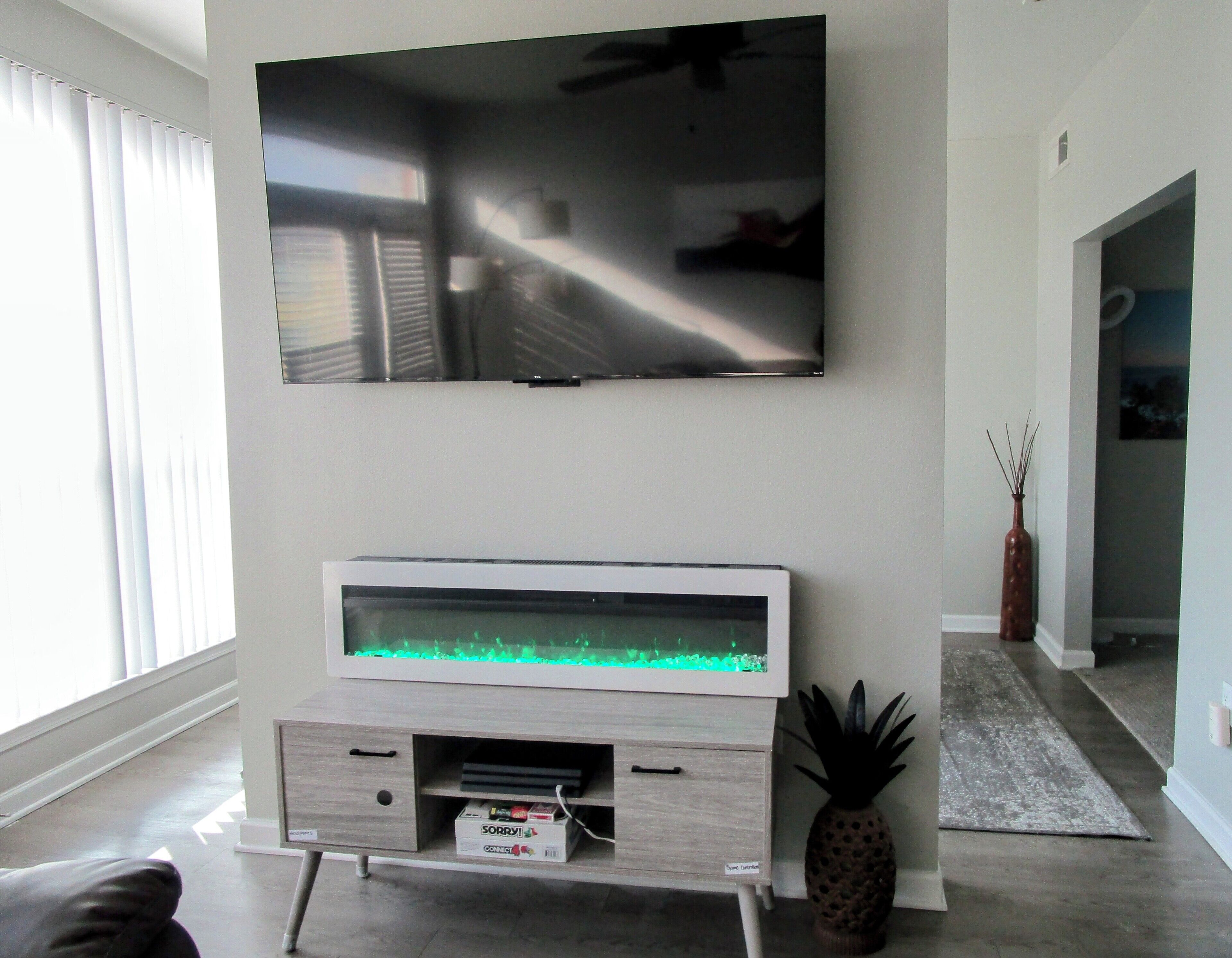 Un soggiorno con una TV a schermo piatto montata a parete, un mobile in legno sottostante e una decorazione a forma di ananas sul pavimento.