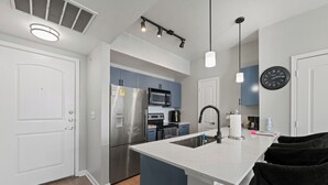 A modern kitchen with white cabinetry, stainless steel appliances, and pendant lighting. - Spacious Dallas Apartment with City Views Near Galleria Mall (Dallas)