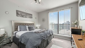 A modern bedroom with a large bed, a ceiling fan, a cityscape view, and a balcony with a railing. - Spacious Dallas Apartment with City Views Near Galleria Mall (Dallas)