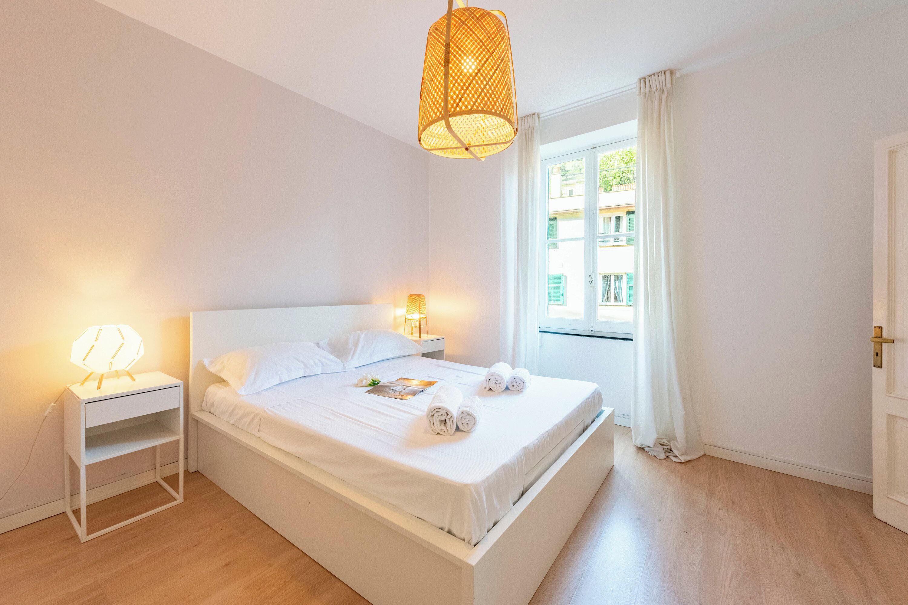 Un dormitorio limpio y luminoso, con cama, lámparas de noche y una ventana con cortinas.