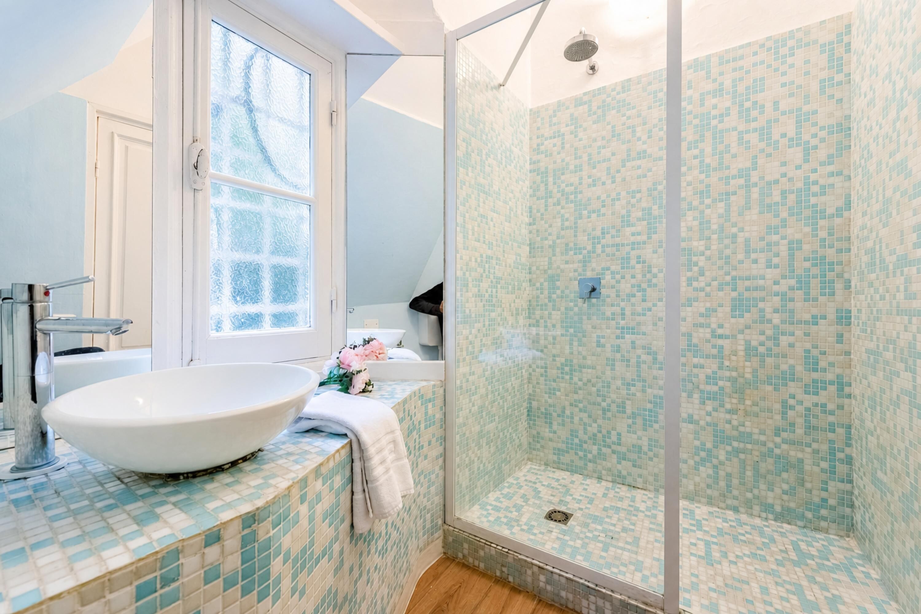 Un baño con un lavabo grande y blanco, ducha con mosaicos y ventana.