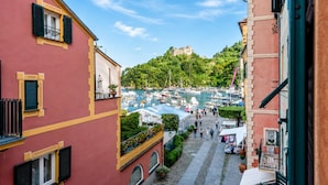 A narrow street with buildings on either side, a marina in the distance, and a hill with a castle-like structure.