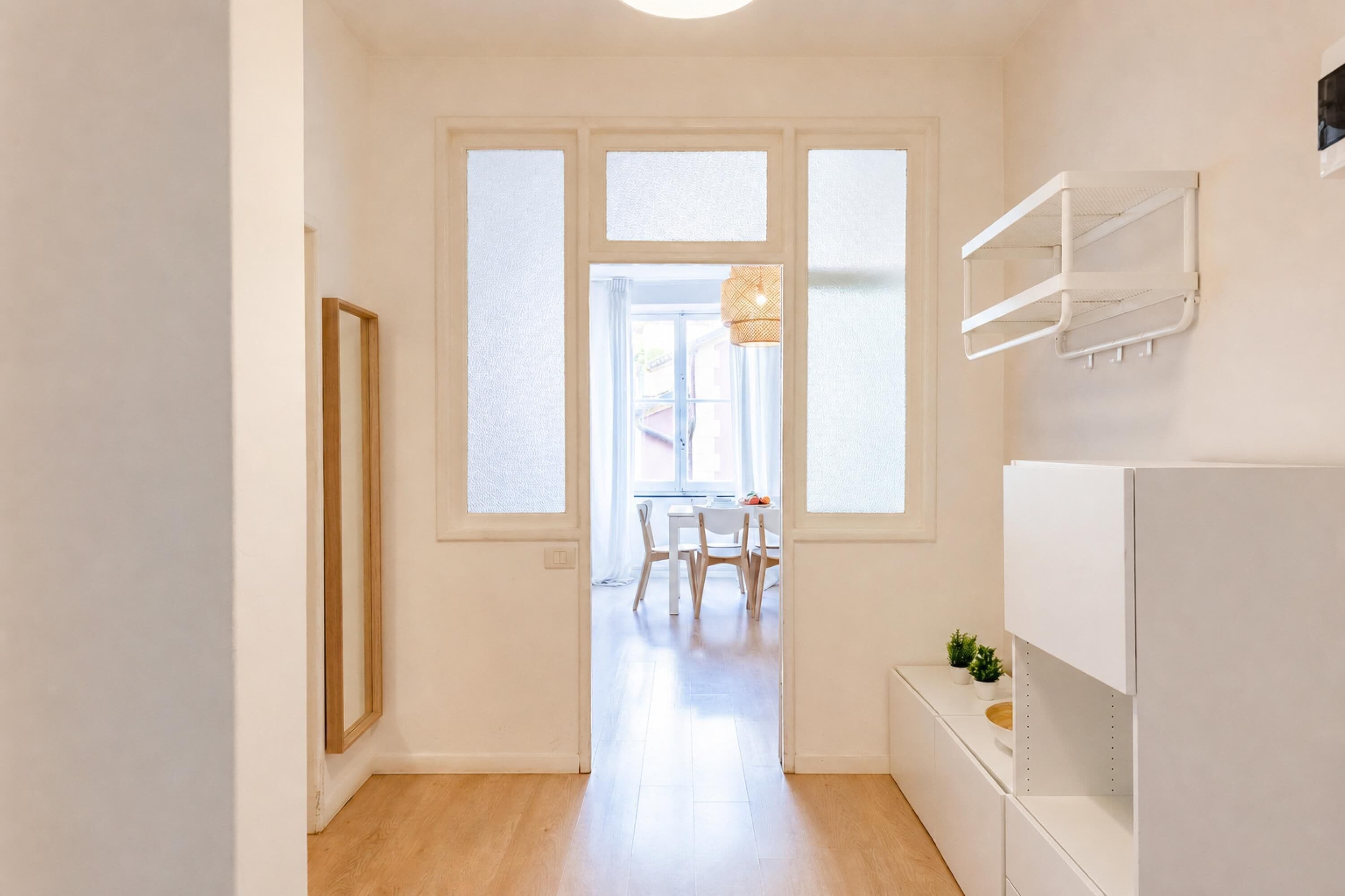 A hallway with a dining area, a white cabinet, and a window with a hanging light fixture.