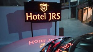 A neon sign for Hotel JRS with a logo and the name illuminated in yellow. - JSR Hotels (Narendranagar)