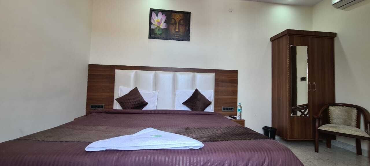 A hotel room with a large bed, a wooden wardrobe, a chair, and a wall-mounted artwork.