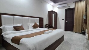 A hotel room with a large bed, a wardrobe, a mirror, and a door with curtains. - JSR Hotels (Narendranagar)