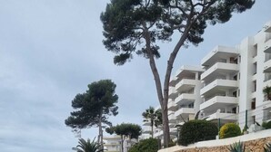 En kystpromenade med en stenvæg, der fører til en strand med store sten og udsigt til en bygning med flere etager og balkoner.