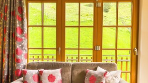 A beige sofa with floral cushions, a wooden door with glass panels, and a view of a green landscape. - Modern Mountain Apart 5 - on skiing slope (Rauris)