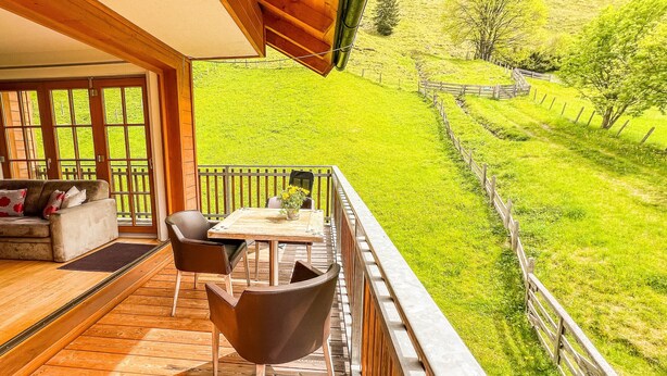 A wooden deck with a sofa and chairs, a table with a vase, and a view of a green landscape with a fence. - Modern Mountain Apart 5 - on skiing slope (Rauris)