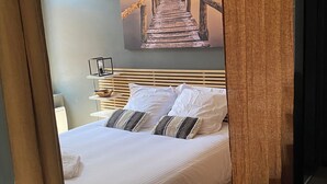 A bedroom with a bed, pillows, a nightstand, a lamp, and a painting of a bridge.