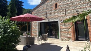 A stone building with a patio area featuring outdoor furniture and a red umbrella.