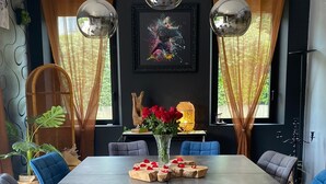 A modern dining room with a large rectangular table, blue and grey upholstered chairs, and two pendant lights.