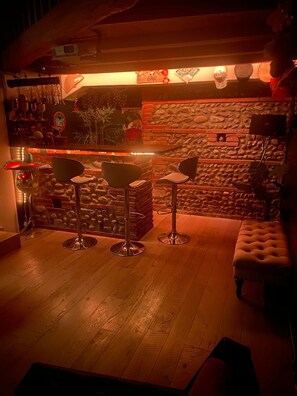 Relax in our inviting bar area with a warm ambiance, featuring a bar, stools, and a cushioned bench.