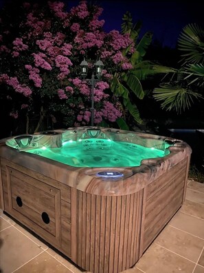 Relax in the outdoor hot tub surrounded by lush greenery and flowering plants.
