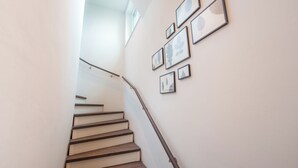 A staircase with wooden steps and a metal handrail, leading to a landing with a white wall and several framed artworks.