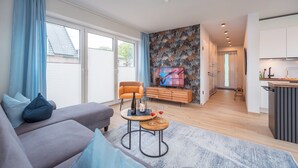 A modern living room with a sofa, a TV, and a small table with wine glasses.