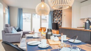 A modern dining area with a wooden table set for four, a sofa, and a kitchen in the background.