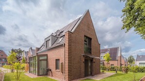 A modern brick house with a sloped roof, large windows, and a well-maintained lawn.