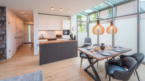 A modern kitchen with a central island, a dining area with a table and chairs, and large windows providing natural light.