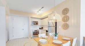 Une cuisine moderne avec des meubles blancs, des appareils en acier inoxydable et un coin repas doté d’une table en bois, mise pour deux personnes.
