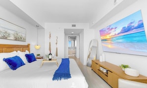 A modern hotel room with a large bed, a bedside table, a TV, and a painting of a sunset over the ocean. - Spectacular Resort, Prime Location, Balcony, Gym (Hallandale Beach)