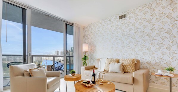 Un salon moderne avec un canapé, des fauteuils, une table basse et une vue sur la ville grâce à de grandes fenêtres.