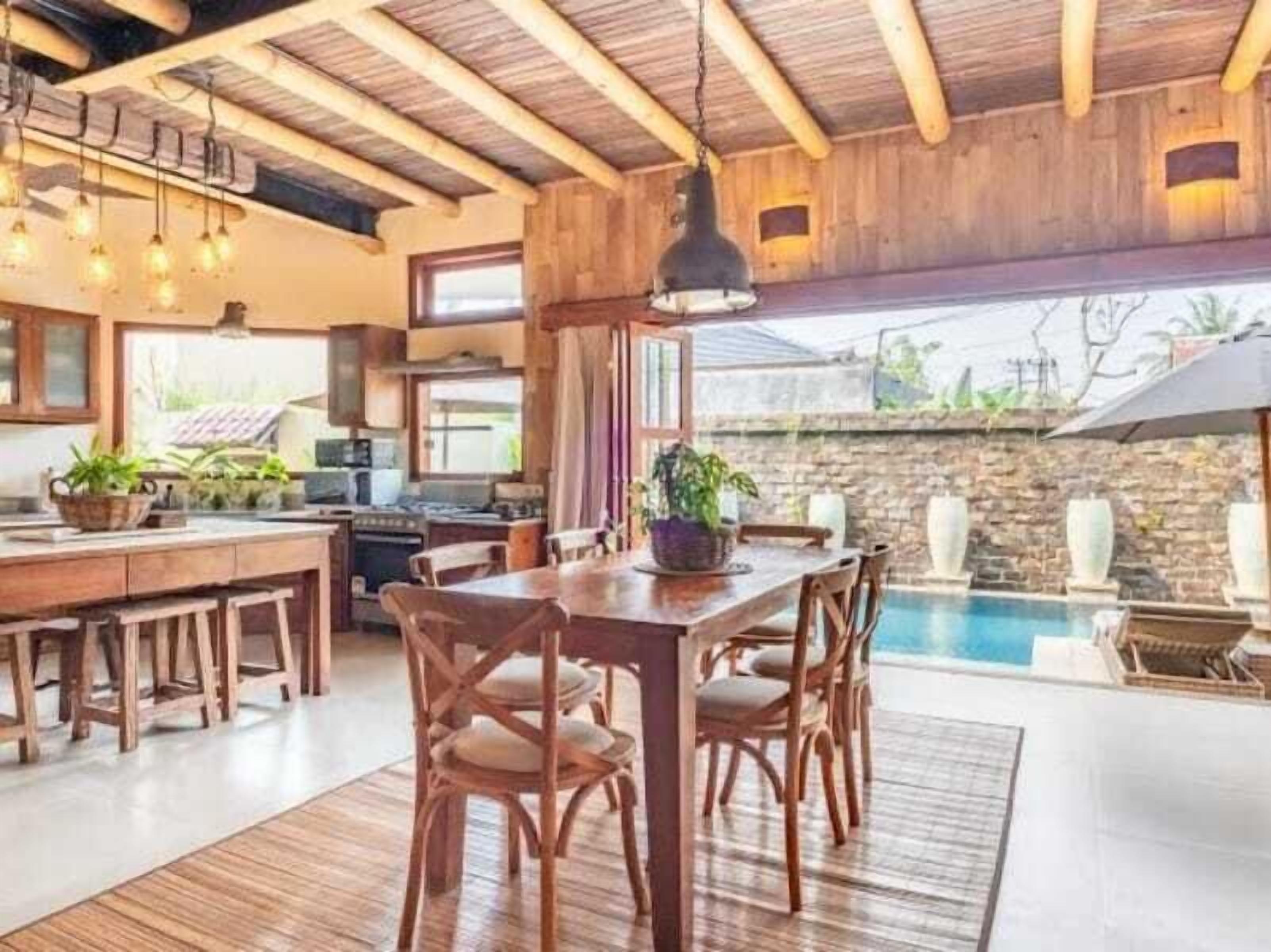 A spacious kitchen with wooden beams, a dining area with a pool view, and a stone wall.