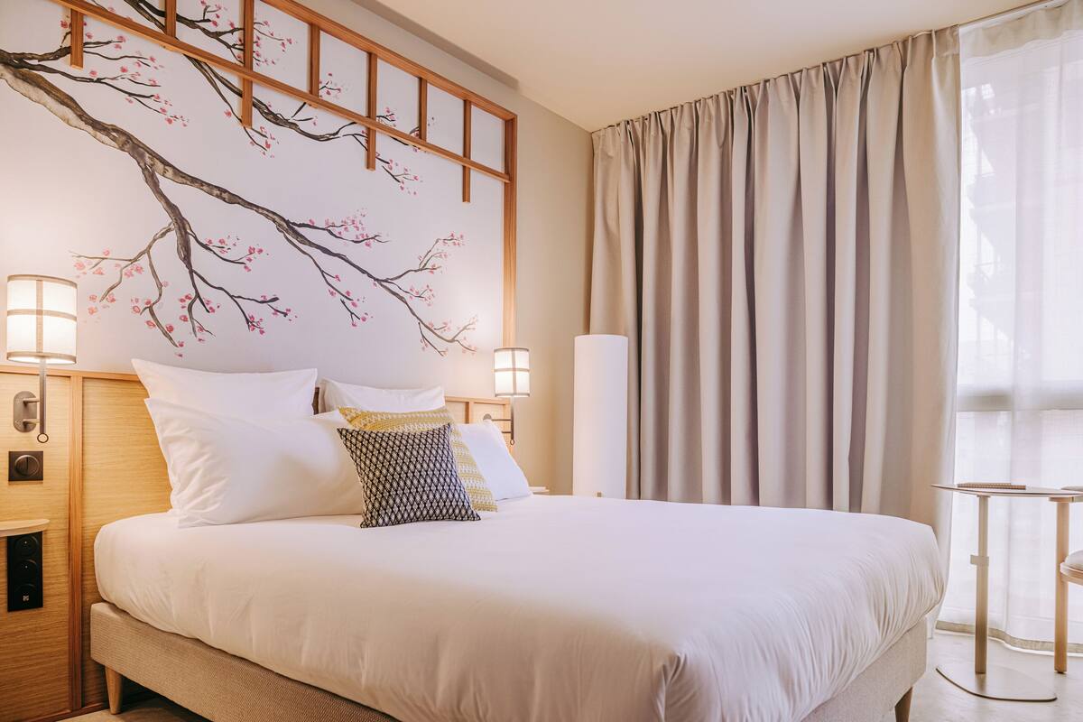 Een hotelkamer met een groot bed, twee bedlampen, een houten hoofdbord en een raam met gordijnen.
