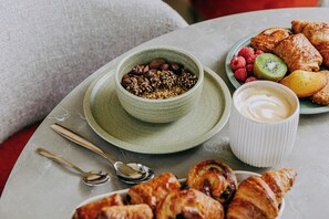 Ein Frühstückstisch mit einer Schüssel Granola, einer Auswahl an Gebäck und einer Tasse Kaffee.
