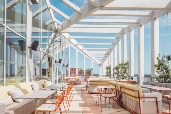 Eine Dachterrasse mit Außenmöbeln, großen Fenstern und freiem Blick auf die Stadtlandschaft.