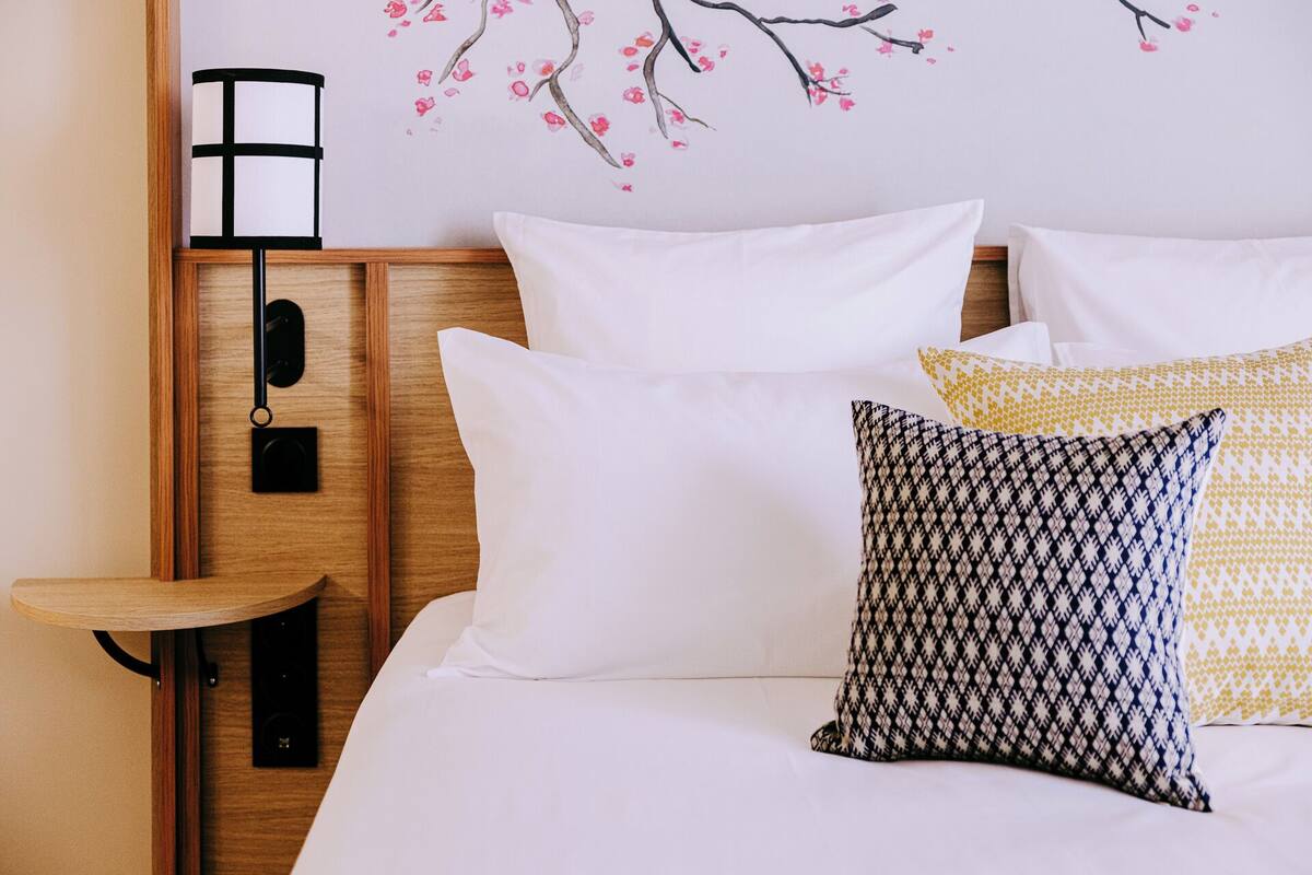 Een hotelkamer met een houten hoofdeinde, wit bedlinnen en een wandlamp.