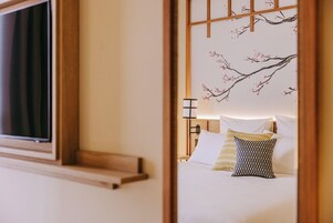 Habitación de hotel con cama, almohadas, mesita de noche y pared decorada con un diseño de cerezos en flor.