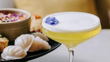 A martini glass with a yellow liquid and a blue flower on the rim, placed on a coaster.